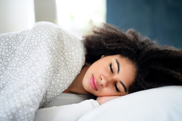 Portrait of young woman with closed eyes indoors, sleeping in bed.