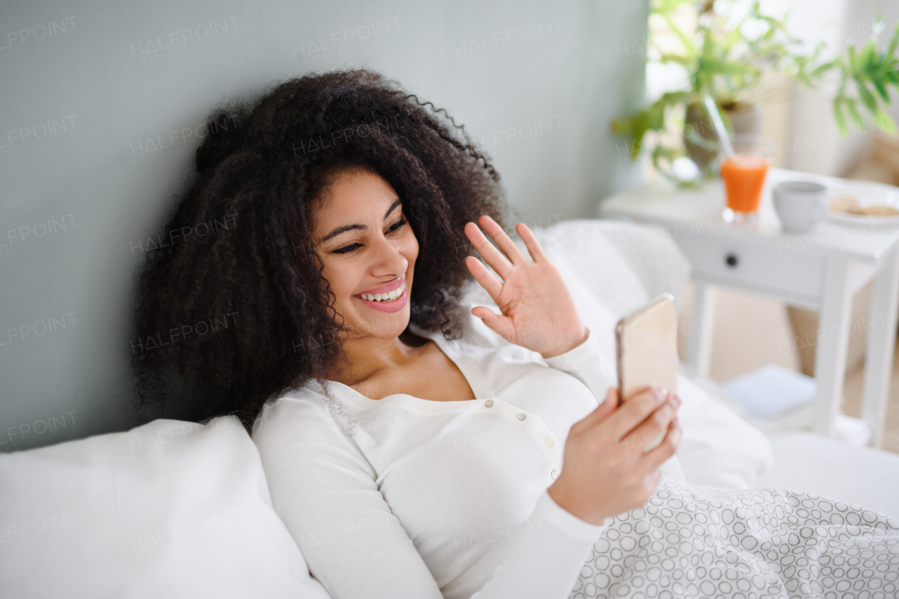 Portrait of cheerful young woman with smartphone indoors on bed, a video call concept.