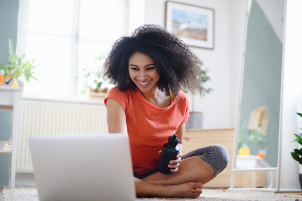 Happy young woman with laptop indoors at home, doing exercise. Sport concept.