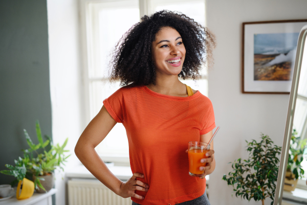 Happy young woman with healthy drink indoors at home, resting after exercise. Sport concept.