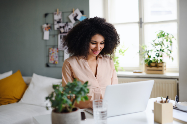 Happy young woman student with laptop working indoors at home, home office concept.