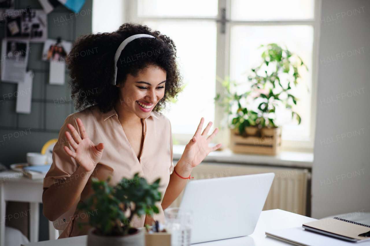 Happy young woman with laptop indoors at home, home office and video call concept.