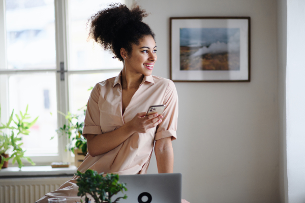 Portrait of young woman with laptop and smartphone indoors at home, home office concept.