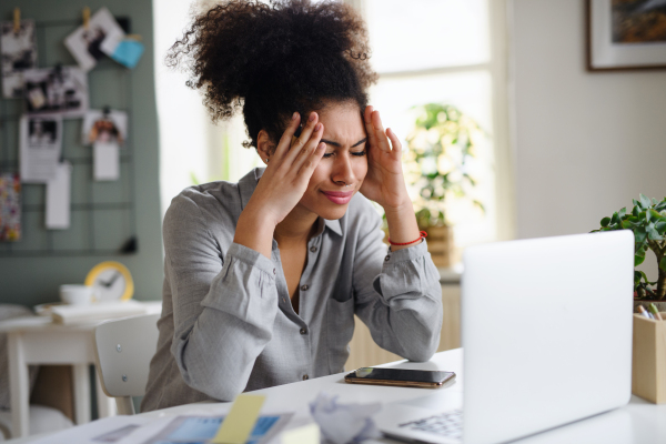 Frustrated young woman with laptop working indoors at home, home office concept.