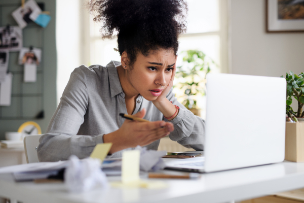 Frustrated young woman with laptop working indoors at home, home office concept.