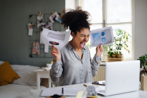 Frustrated young woman with laptop working indoors at home, home office concept.