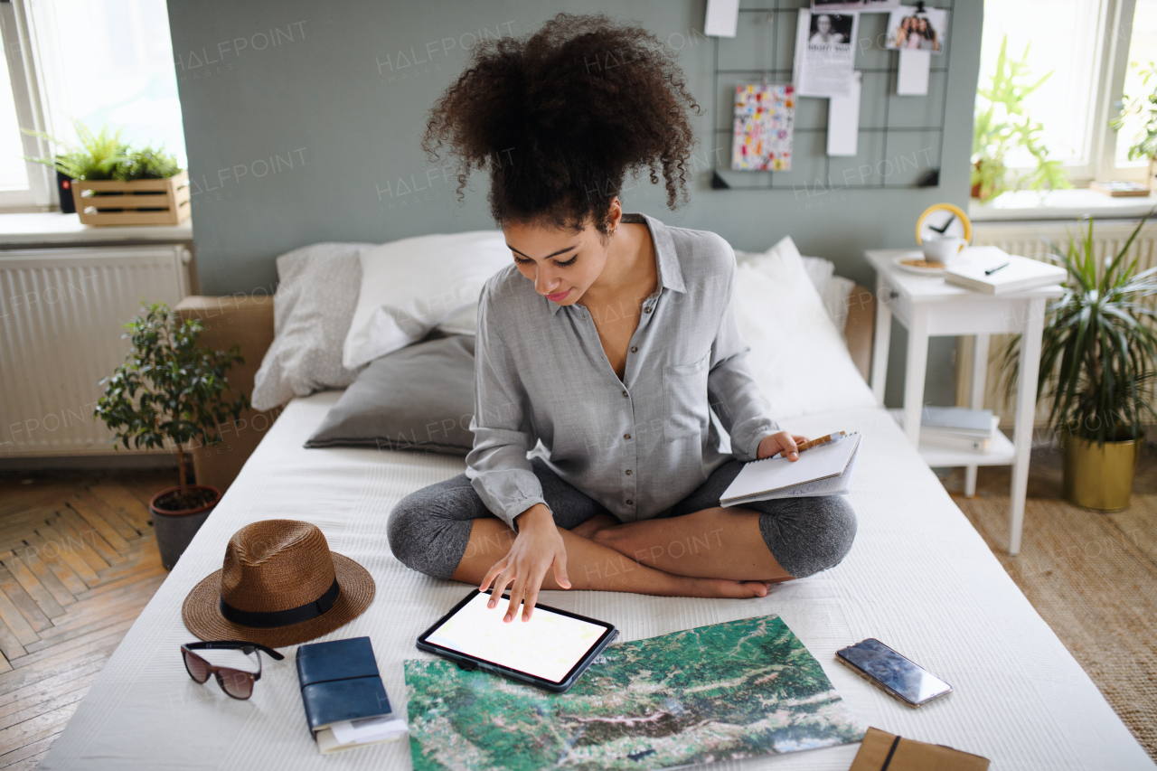 Happy young woman with tablet and map indoors at home, planning traveling trip.