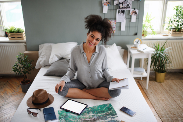 Happy young woman with tablet and map indoors at home, planning traveling trip.