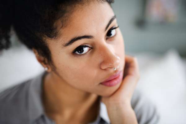 Close-up front view portrait of sad beautiful young woman indoors, looking at camera.