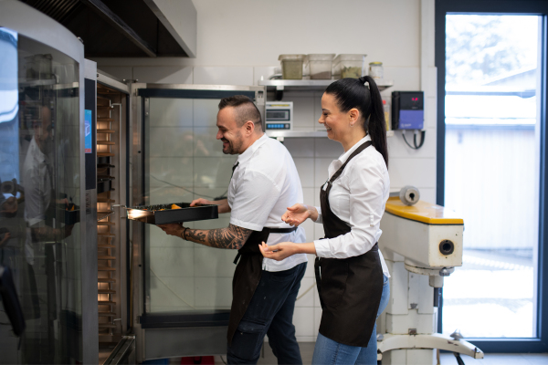 A happy chef and cook working on their dishes indoors in restaurant kitchen.