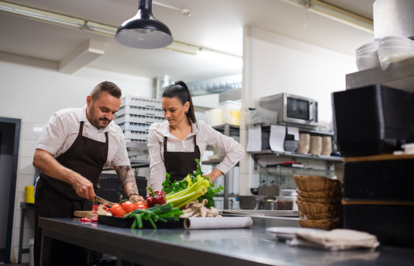 A chef teaching how to cook, cutting vegetables indoors in commercial kitchen.