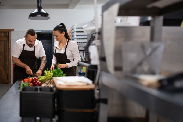 A chef teaching how to cook, cutting vegetables indoors in commercial kitchen.
