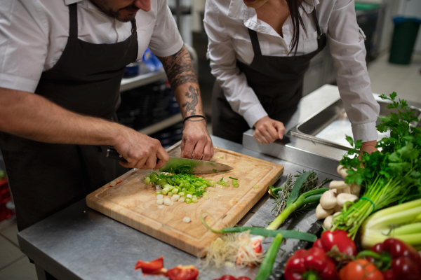 An unrecognizable chef teaching how to cook, cutting vegetables indoors in commercial kitchen.