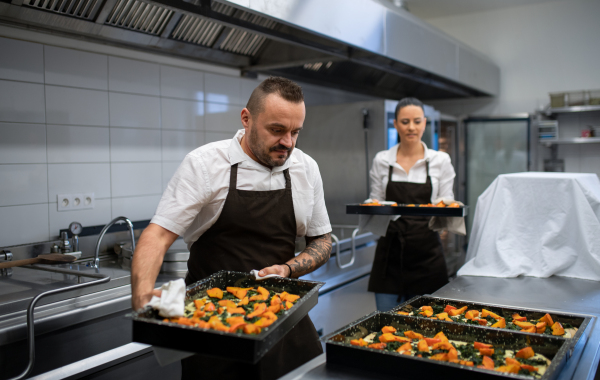A chef and cook working on their dishes indoors in restaurant kitchen.