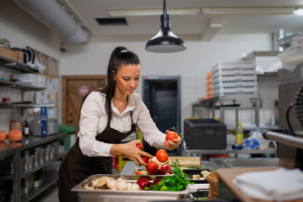 A professional female chef cutting vegetables indoors in restaurant kitchen.