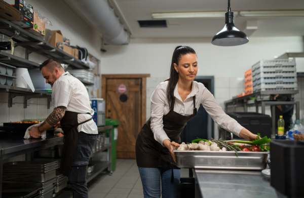 A chef and cook working on their dishes indoors in restaurant kitchen.