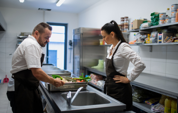 A cook washing vegetables in sink in commercial kitchen.
