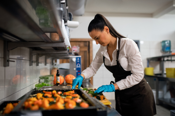 A professional chef working on her dishes indoors in restaurant kitchen.