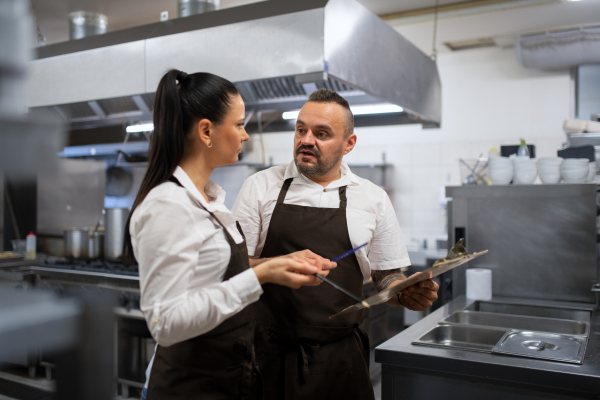 A chef and cook discussing menu indoors in restaurant kitchen.