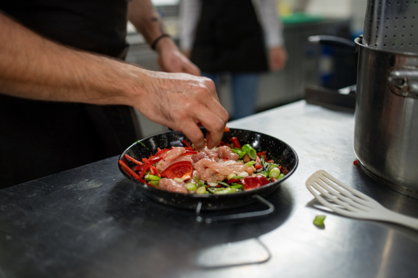 An unrecognizable chef preparing meal indoors in restaurant kitchen.