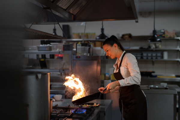 A professional chef preparing meal, flambing indoors in restaurant kitchen.