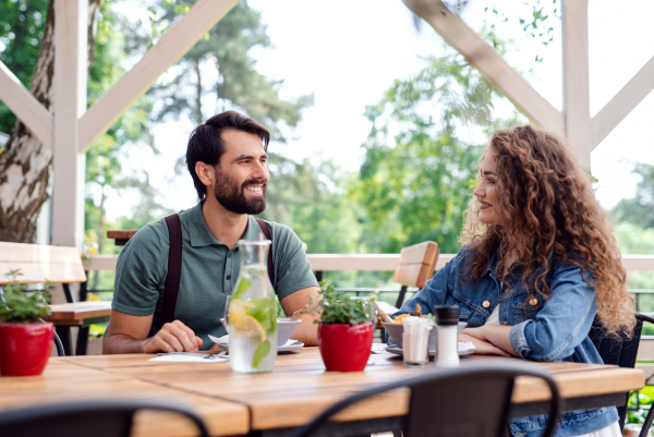 Happy couple sitting at the table outdoors on terrace restaurant, talking.