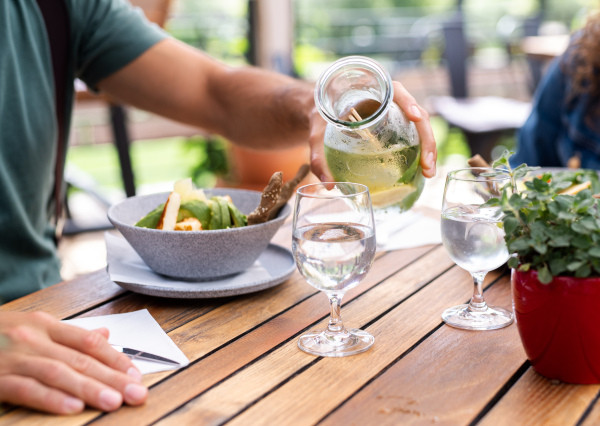 Midsection of young couple sitting outdoors on terrace restaurant, having lunch.