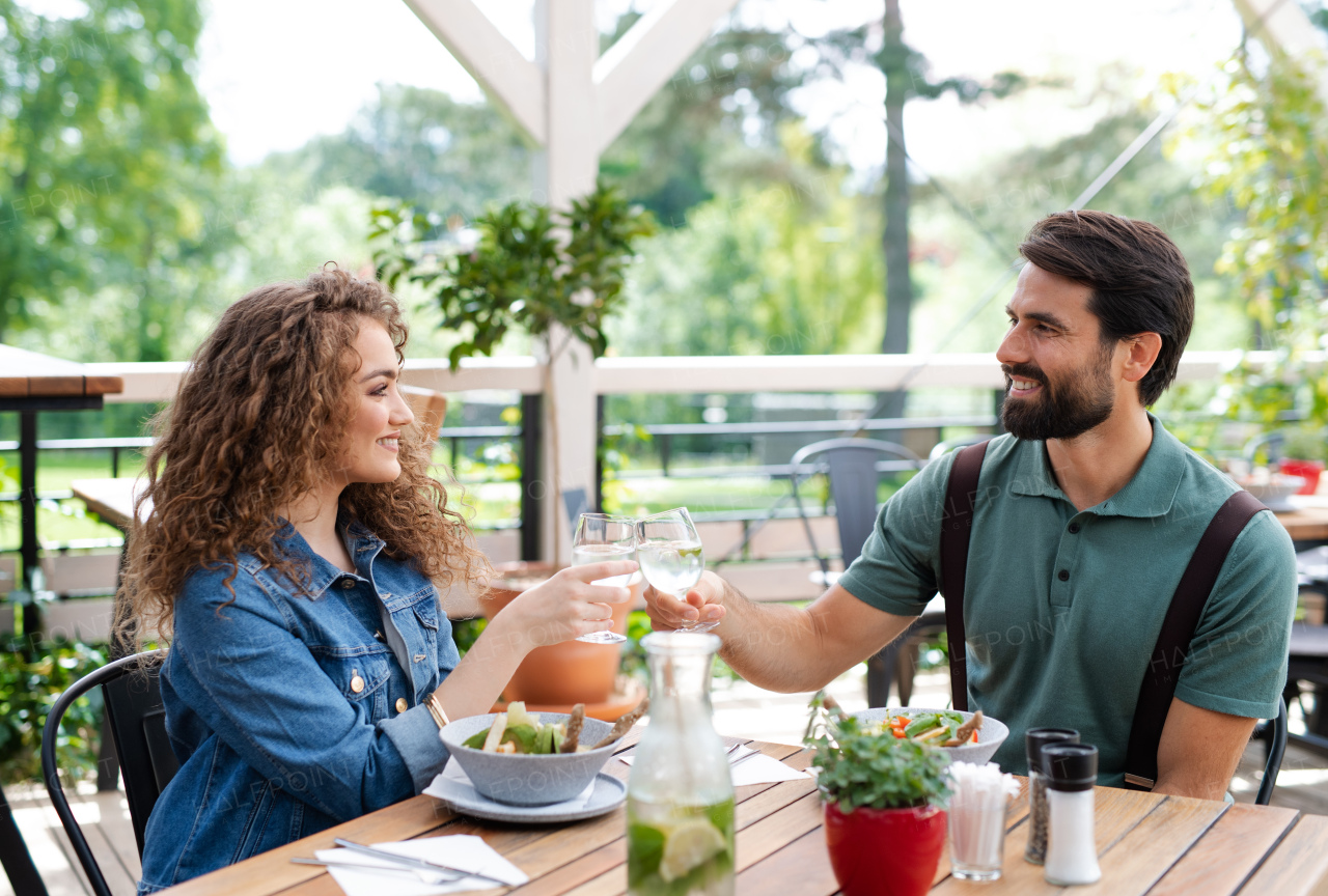 Happy young couple sitting outdoors on terrace restaurant, clinking glasses.