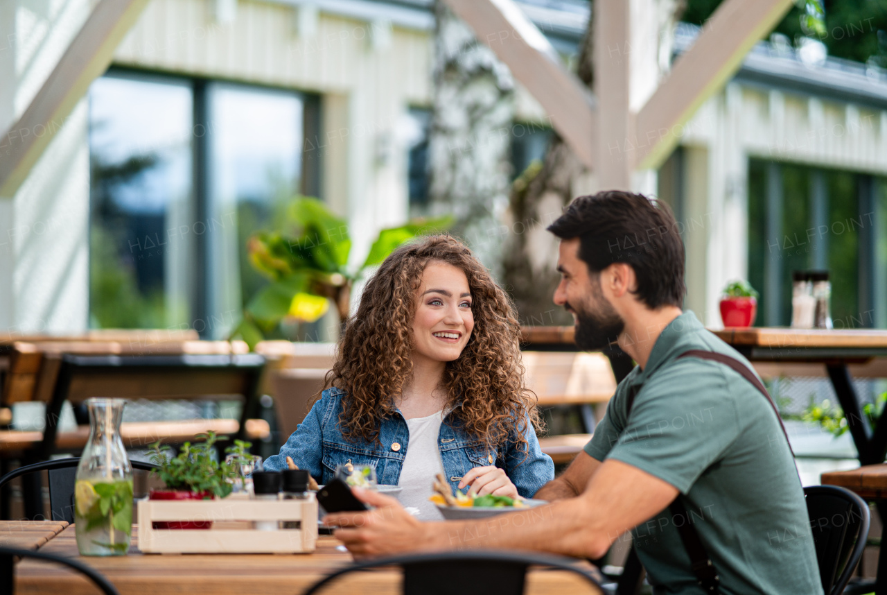 Happy young couple sitting outdoors on terrace restaurant, talking.