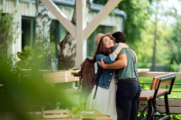 Happy young couple greeting outdoors on terrace restaurant, hugging.