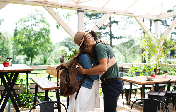 Happy young couple greeting outdoors on terrace restaurant, hugging.