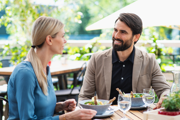 Happy couple sitting at the table outdoors on terrace restaurant, talking.