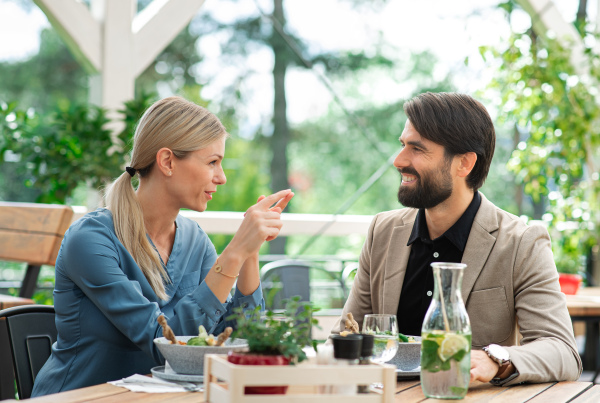 Happy couple sitting at the table outdoors on terrace restaurant, talking.