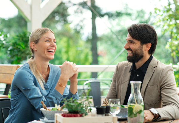 Happy couple sitting at the table outdoors on terrace restaurant, talking.