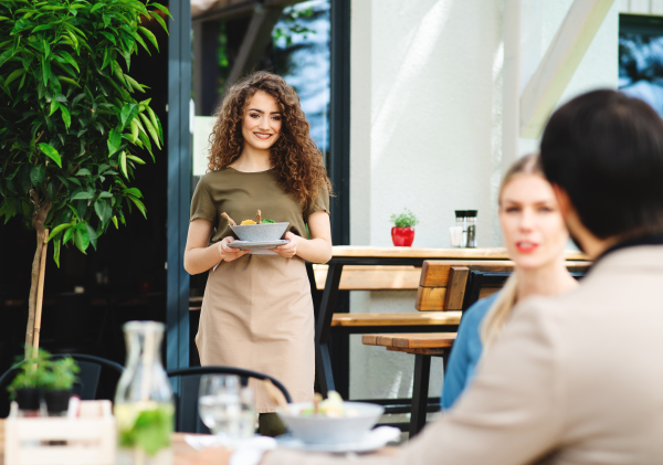 Woman waitress serving happy couple outdoors on terrace restaurant.