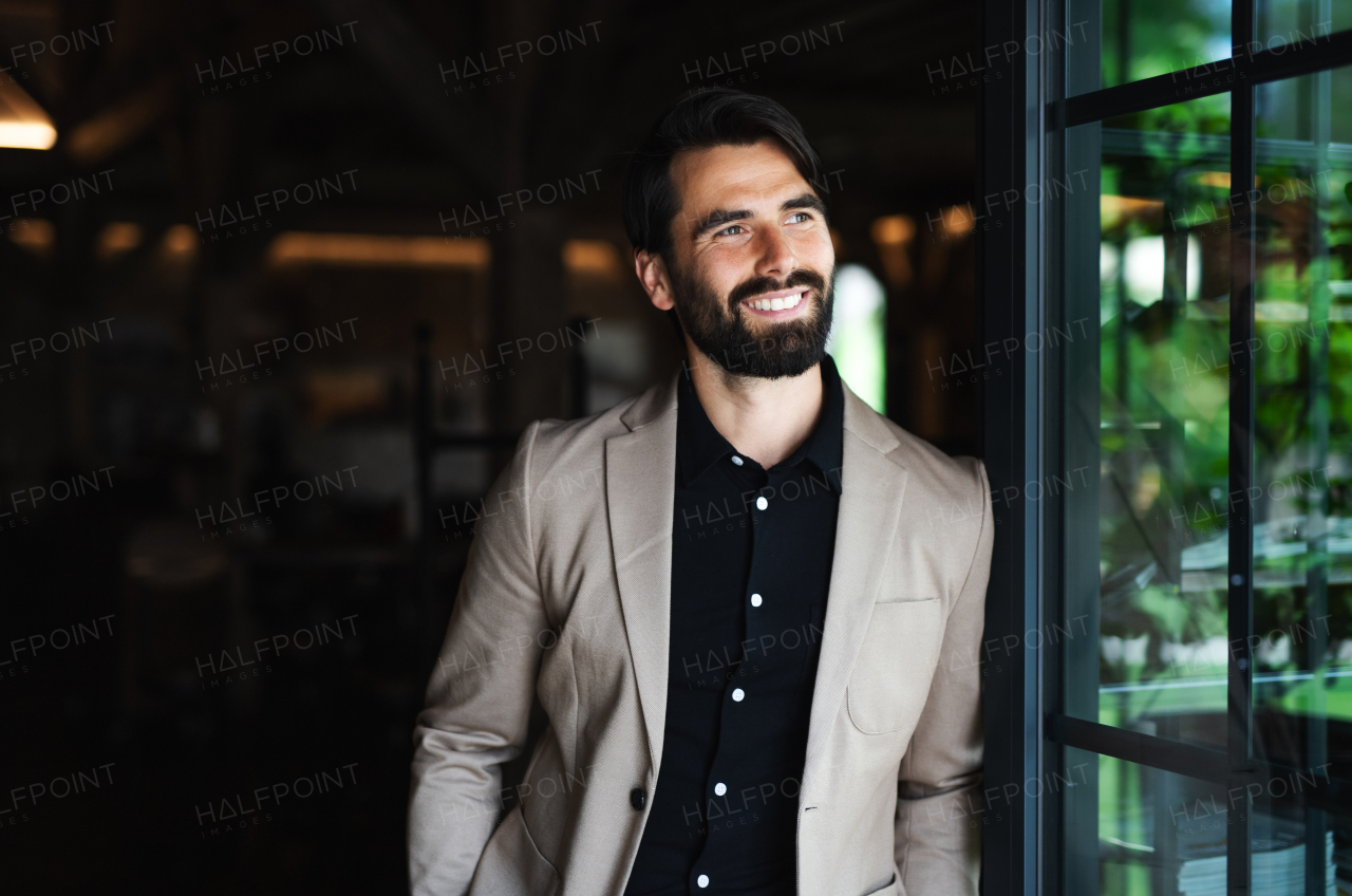 Portrait of businessman with jacket standing indoors in restaurant, looking out.