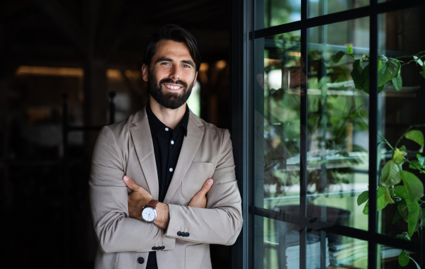 Portrait of businessman with jacket standing indoors in restaurant, looking at camera.