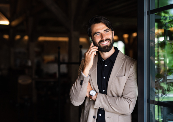 Front view portrait of businessman with jacket standing indoors in restaurant, using telephone.