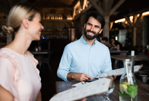 Happy couple sitting indoors in restaurant, looking at menu and talking.