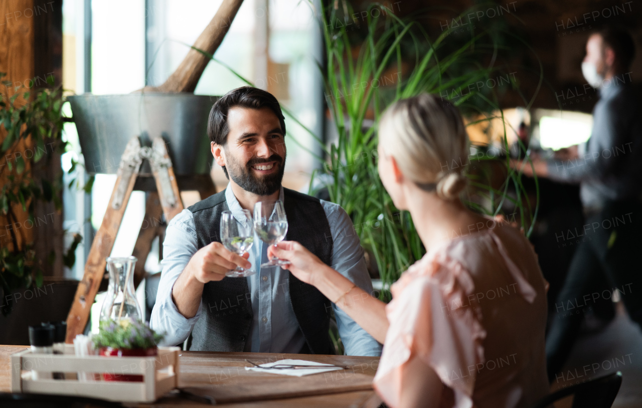 A happy couple sitting indoors in restaurant, clinking glasses.