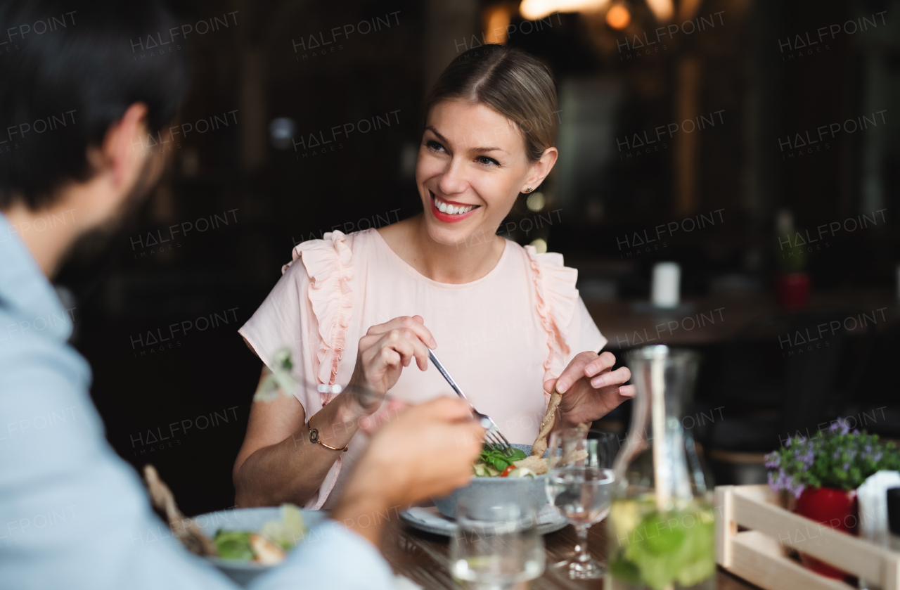 A happy couple sitting indoors in restaurant, eating.