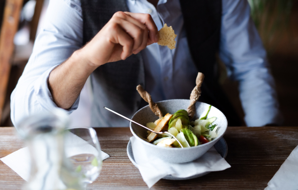 Midsection of unrecognizable man sitting indoors in restaurant, eating.