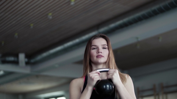 A portrait of a beautiful young girl or woman doing exercise with a kettlebell in a gym.