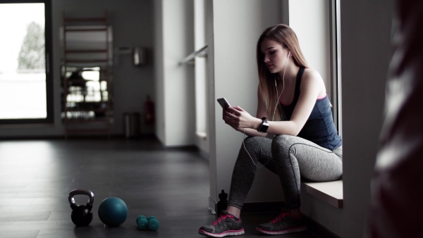 A young girl or woman with earphones, smartphone and smartwatch in a gym.