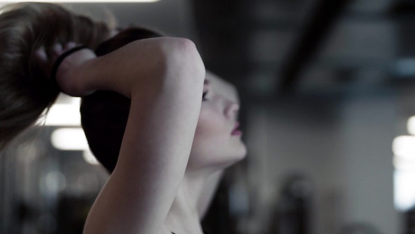 A portrait of a beautiful young girl or woman standing in a gym, doing a ponytail.