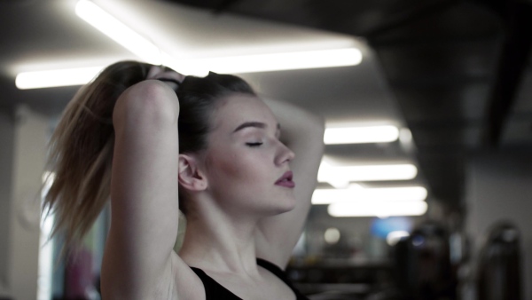 A portrait of a beautiful young girl or woman standing in a gym, doing a ponytail.