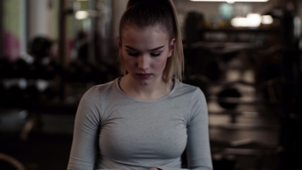 Young girl or woman putting on fingerless gloves in gym.