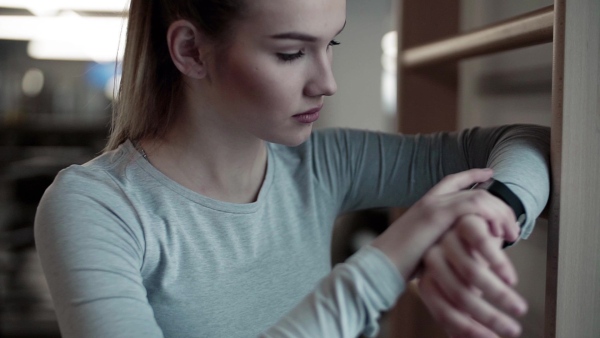 A young girl or woman in a gym, using smartwatch. Slow motion.