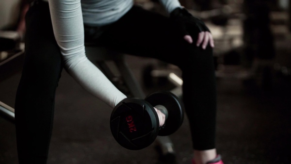 A young girl or woman with dumbbells, doing workout in a gym. Slow motion.