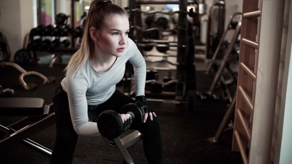 A young girl or woman with dumbbells, doing workout in a gym. Slow motion.